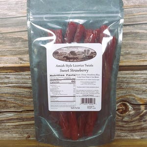 May include: A transparent bag containing red Amish-style licorice twists. The label displays "Millstone Acres Amish Style Licorice Twists Sweet Strawberry." The bag is sealed and set against a wooden backdrop.