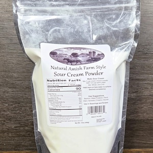 May include: A clear plastic bag containing white sour cream powder. The label reads "Natural Amish Farm Style Sour Cream Powder" with a picture of a horse-drawn carriage. The bag contains 13oz (369g) of powder.