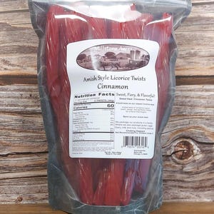 May include: A transparent bag containing red Amish-style licorice twists. The label displays "Millstone Acres Amish Style Licorice Twists Cinnamon." Nutritional information is also shown. The bag is sealed and rests on a wooden surface.