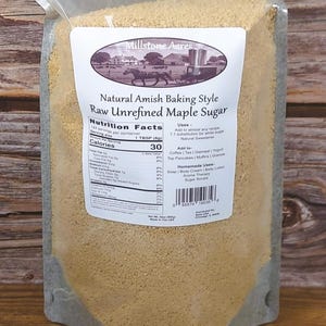 Puede incluir: Una bolsa transparente llena de azúcar de arce crudo sin refinar. La etiqueta dice "Natural Amish Baking Style" e incluye información nutricional. La bolsa tiene una etiqueta con una escena rural y la marca "Millstone Acres."