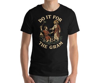 May include: Black t-shirt featuring a graphic of a religious scene with the text "DO IT FOR THE GRAM". The design depicts a figure in water reaching for another figure. The text is in a stylized font.