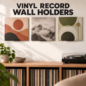 Peut inclure: Trois supports muraux noirs en métal pour disques vinyles fixés au mur, présentant chacun une pochette d'album carrée. La pochette de gauche montre un soleil et un paysage orange, celle du centre une montagne, et celle de droite des cercles verts.