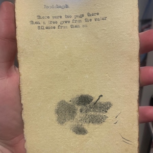 May include: A vintage-style, rectangular paper with the text "Roodaberuh" and a poem about pugs and a tree. A black ink drawing of a tree is at the bottom. The paper has a yellowed, aged appearance.