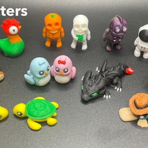 Puede incluir: Una colección de figuras de personajes coloridas y hechas a mano. Las figuras incluyen un oso con un corazón, pájaros, tortugas, un dragón y un astronauta. La palabra "Characters" está escrita en texto blanco en la parte superior de la imagen.