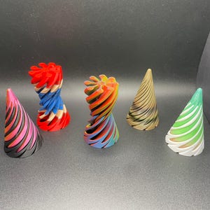 May include: A collection of six colorful, abstract decorative objects. The objects include three cone-shaped pieces with black and pink, green and white, and brown and tan stripes. There are also three spiral-shaped objects in red, white, and blue, and rainbow colors.