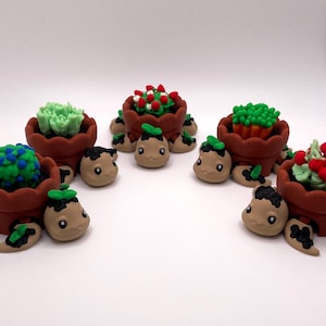 以下が含まれることがあります： 茶色の植木鉢を背負った5体の小さな粘土製のカメのフィギュア。鉢の中には、緑色の多肉植物、赤い花のサボテン、オレンジ色の先端を持つ植物など、細部まで作り込まれた様々な彫刻の植物が入っています。