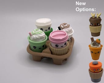 May include: A set of four miniature beverage cups with smiling faces in a brown cardboard carrier, plus three additional cup options on the right labeled New Options. The cups feature lids, whipped cream toppings, and textured sleeves.
