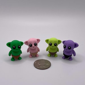 May include: Four small, colorful alien figurines in green, pink, lime green, and purple. Each figure has large black eyes and small brown or black diaper-like bottoms. A quarter is next to the figurines for size comparison.