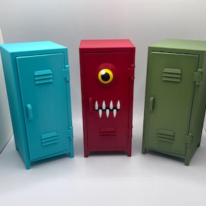 May include: Three colorful miniature lockers. A teal blue locker, a red locker with a single yellow-eyed monster face, and a green locker. Each has a handle and vent details.
