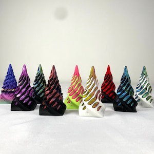 May include: A collection of nine conical sculptures featuring a spiraling, ribbed design. Each piece displays a unique color combination, including purple, pink, black, red, blue, green, and white, with some featuring dual-tone gradients.