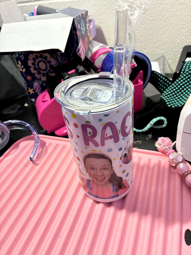 Puede incluir: Un vaso de acero inoxidable con tapa y pajita transparente. El vaso est&aacute; decorado con una foto de una mujer y el nombre "Grace" en lunares de colores. Se encuentra sobre una alfombrilla rosa acanalada.