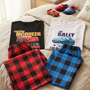 May include: Two sets of pajamas featuring Disney Cars characters. One set includes a black t-shirt with Lightning McQueen and red plaid pants. The other set features a white t-shirt with Sally and blue plaid pants, accompanied by matching character slippers.