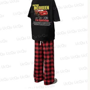 May include: A black short-sleeved t-shirt featuring a graphic of Lightning McQueen with the text "LIGHTNING MCQUEEN" and "I'm lightning" paired with red and black buffalo plaid pajama pants that have a white drawstring at the elastic waistband.