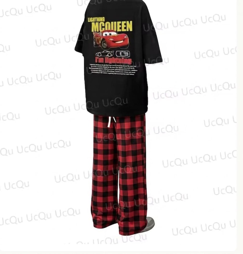 May include: A black short-sleeved t-shirt featuring a graphic of Lightning McQueen with the text "LIGHTNING MCQUEEN" and "I'm lightning" paired with red and black buffalo plaid pajama pants that have a white drawstring at the elastic waistband.
