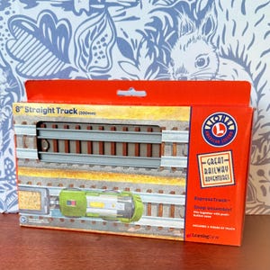 May include: A boxed set of Lionel 200mm straight track pieces. The packaging is red and features the Lionel American Legend logo and the words "Great Railway Adventures." The box also shows a train car and track assembly.