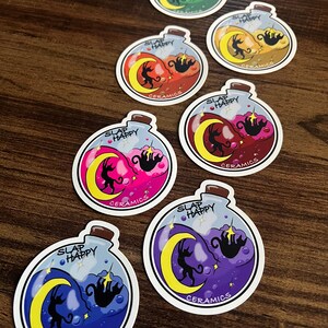 May include: A collection of circular stickers featuring a potion bottle design. Each sticker has a different color scheme, including green, yellow, red, pink, and purple. The stickers have the text "SLAP HAPPY" and "CERAMICS".
