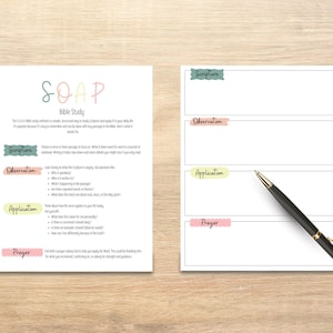 May include: Two white sheets of paper with the text "SOAP Bible Study" and a pen. One sheet details the SOAP method, the other has sections for Scripture, Observation, Application, and Prayer. The pen is black and gold.