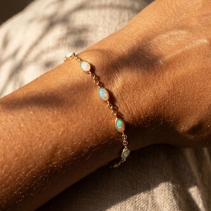 Könnte beinhalten: Ein goldfarbenes Kettenarmband mit einer Reihe kleiner, ovaler, schillernder Opale, die in Metallfassungen eingefasst sind. Das Armband besteht aus feinen goldenen Gliedern, die jeden einzelnen Opalstein in einem durchgehenden Muster verbinden.