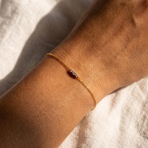 May include: A delicate gold chain bracelet featuring three small, clear, round-cut stones set in a horizontal row. The bracelet is constructed with a fine, polished link chain that encircles the wrist, showcasing a minimalist and refined design.