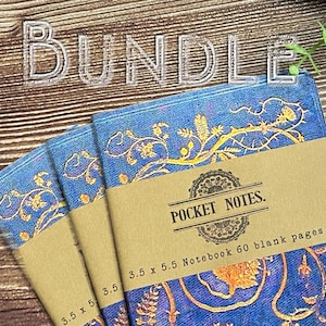 May include: Three blue notebooks with gold floral patterns, each featuring a brown paper band labeled POCKET NOTES. The band displays the text 3.5 x 5.5 Notebook 60 blank pages. The notebooks are arranged in a fan shape on a wood grain surface.