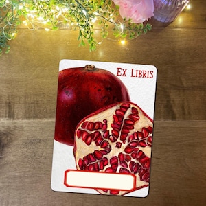 May include: A rectangular card with a watercolour illustration of a pomegranate, whole and sliced, showing seeds. The text "EX LIBRIS" is at the top, and a blank space for personalization is at the bottom.