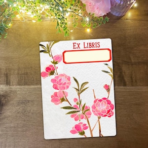 May include: A rectangular white Ex Libris bookplate with a red border and the text "EX LIBRIS" in red. The bookplate features a watercolour illustration of pink flowers and green leaves.