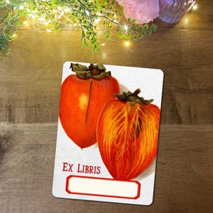 May include: A white Ex Libris card with a vintage illustration of two persimmons, one cut open to reveal the inside. The card has a red border and a space for a name. The text "EX LIBRIS" is printed at the bottom.