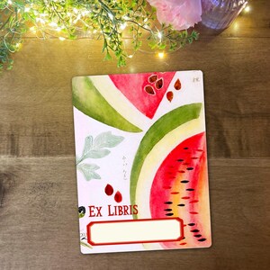 May include: A rectangular bookplate with a watercolour design of watermelon slices and seeds. The words "EX LIBRIS" are printed at the bottom, with a blank space for personalisation. The design includes green leaves and a red border.