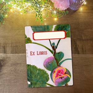 May include: A decorative bookplate featuring a fig illustration. The bookplate has a white background with a fig tree design in green, pink, and yellow. The text "EX LIBRIS" is in red, with a blank label at the top.