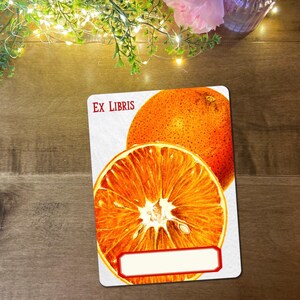 May include: A rectangular card with an orange fruit illustration. The card features a whole orange and a cross-section of an orange. The words "EX LIBRIS" are printed in red at the top. A white rectangle with a red border is at the bottom.