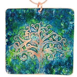 May include: A copper-colored tree pendant necklace. The square pendant features a textured background of blue and green hues. The tree design is in a copper color, with intricate branches and a detailed trunk. The necklace has a delicate copper chain.