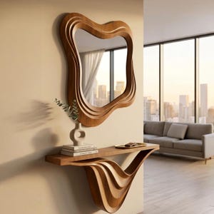 May include: A wooden, wavy-edged mirror hangs above a matching console table. The mirror and table have a warm, brown finish. A small vase with greenery and a stack of books sit on the table. The room has a modern design with a city view.
