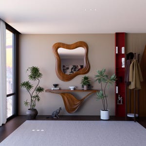 Könnte beinhalten: Ein modernes Interieur mit einer Holzkonsolentisch und einem wellenförmigen Spiegel. Der Raum umfasst ein rotes Bücherregal, Topfpflanzen und eine graue Katze. Ein Kleiderständer mit Mänteln und ein Fenster mit Aussicht sind ebenfalls sichtbar. Einzigartiges Design.