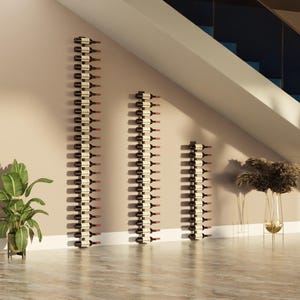 May include: Three wooden wine racks mounted on a beige wall, each holding multiple wine bottles. The racks vary in height, creating a visually appealing display. A potted plant and decorative vase are also present.