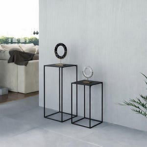 Può includere: Due espositori in metallo nero di diverse altezze, ciascuno con un piano quadrato. Uno stand ospita un anello decorativo nero e oro, l'altro un anello decorativo bianco e oro. Gli stand sono di fronte a un muro bianco.