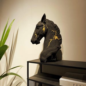 May include: Black horse head sculpture with gold accents. The sculpture is displayed on a black metal shelf. The horse head is a bust, showing the head and neck. The sculpture has a textured surface.