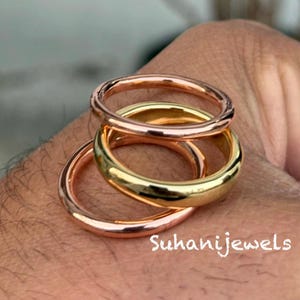 May include: Three rings in rose gold and yellow gold are stacked together. The rings are smooth and shiny, with a rounded design. The text "Suhanijewels" is visible in the image.