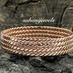 May include: Rose gold-colored stackable rings with a twisted rope design. The rings are displayed on a dark, textured surface. The text "suhanijewels" is visible in the image.