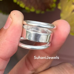 Puede incluir: Tres anillos de plata apilados, mostrando una variedad de diseños. Los anillos se sostienen en una mano, con el texto "SuhaniJewels" visible. Los anillos tienen una superficie pulida y reflectante.