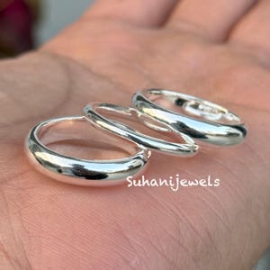 May include: Three silver rings with a polished finish. The rings are different sizes and are stacked together. The text "Suhanijewels" is visible on the surface.
