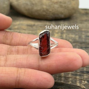 May include: A silver ring featuring a raw, rectangular, deep red gemstone. The ring has a split shank design. The text "suhanijewels" is visible in the image.