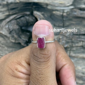 May include: A sterling silver ring featuring a rectangular, deep pink ruby gemstone. The ring's band is thin and polished, and the gemstone is set in a simple bezel. The text "suhanijewels" is visible.