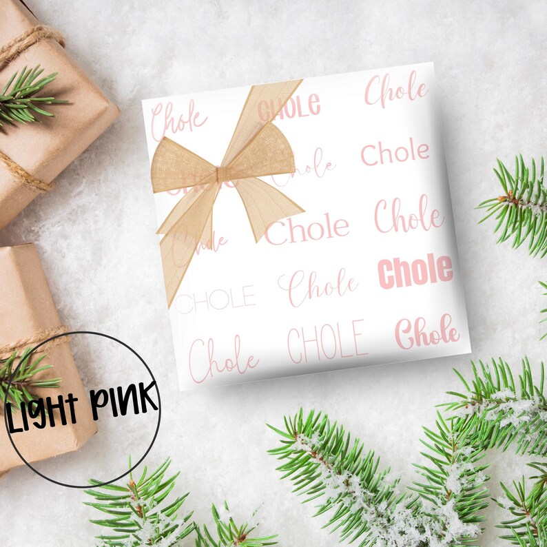 May include: White gift wrap with a repeating pattern of the word "Chole" in light pink. A light brown ribbon is tied on top. The words "LIGHT PINK" are in a black circle in the lower left corner.