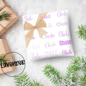 May include: White gift wrap with the word "Chole" in a repeating pattern of lavender script. A tan ribbon bow is tied on top. The word "Lavender" is in a black circle in the lower left corner.