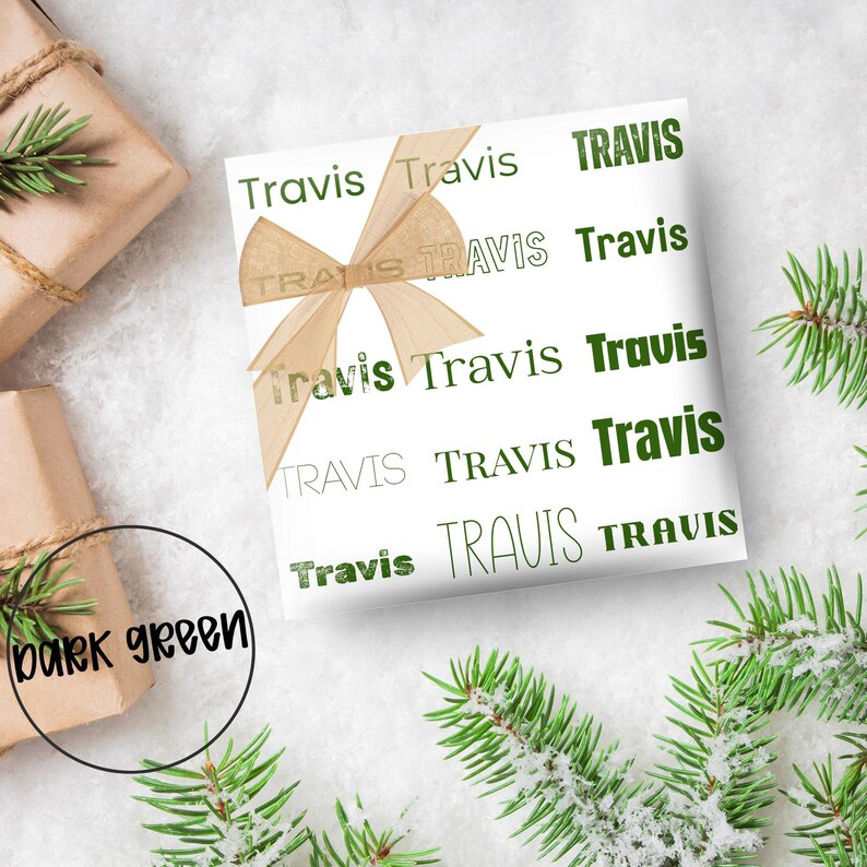 May include: White gift wrap with the name "Travis" printed in dark green. A tan ribbon is tied on top. The words "dark green" are in a circle in the lower left corner. Green pine branches are in the background.