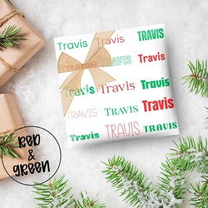 May include: White gift wrap with the name "Travis" repeated in red and green. A tan bow adorns the wrapped gift. The words "Red & Green" are in a circle in the lower left corner. Evergreen branches are in the background.