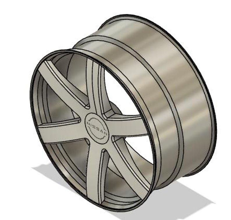 May include: A silver-colored alloy wheel with a multi-spoke design. The wheel features the brand name "NISSAN" in the center. The wheel is designed for a vehicle and is shown at an angle, casting a shadow.