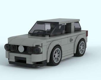 May include: A light gray toy car constructed from interlocking blocks. The car features a boxy design with black windows, silver wheels, and a black front bumper. The headlights are black and round. The car is a model of a station wagon.