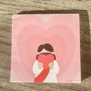 Könnte beinhalten: Quadratischer, rosa Haftzettel mit einer Cartoon-Illustration einer Figur, die ein rotes Herz hält. Die Figur trägt ein weißes Gewand und hat braune Haare. Der Hintergrund zeigt konzentrische rosa Herzen. Die Signatur des Künstlers befindet sich in der unteren rechten Ecke.