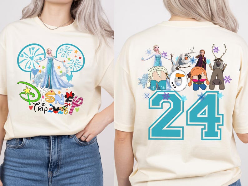 May include: Cream-colored t-shirt featuring a Disney Trip design with Elsa and fireworks. The back of the shirt displays the number 24 in teal, along with various Frozen characters. A fun and colorful design.